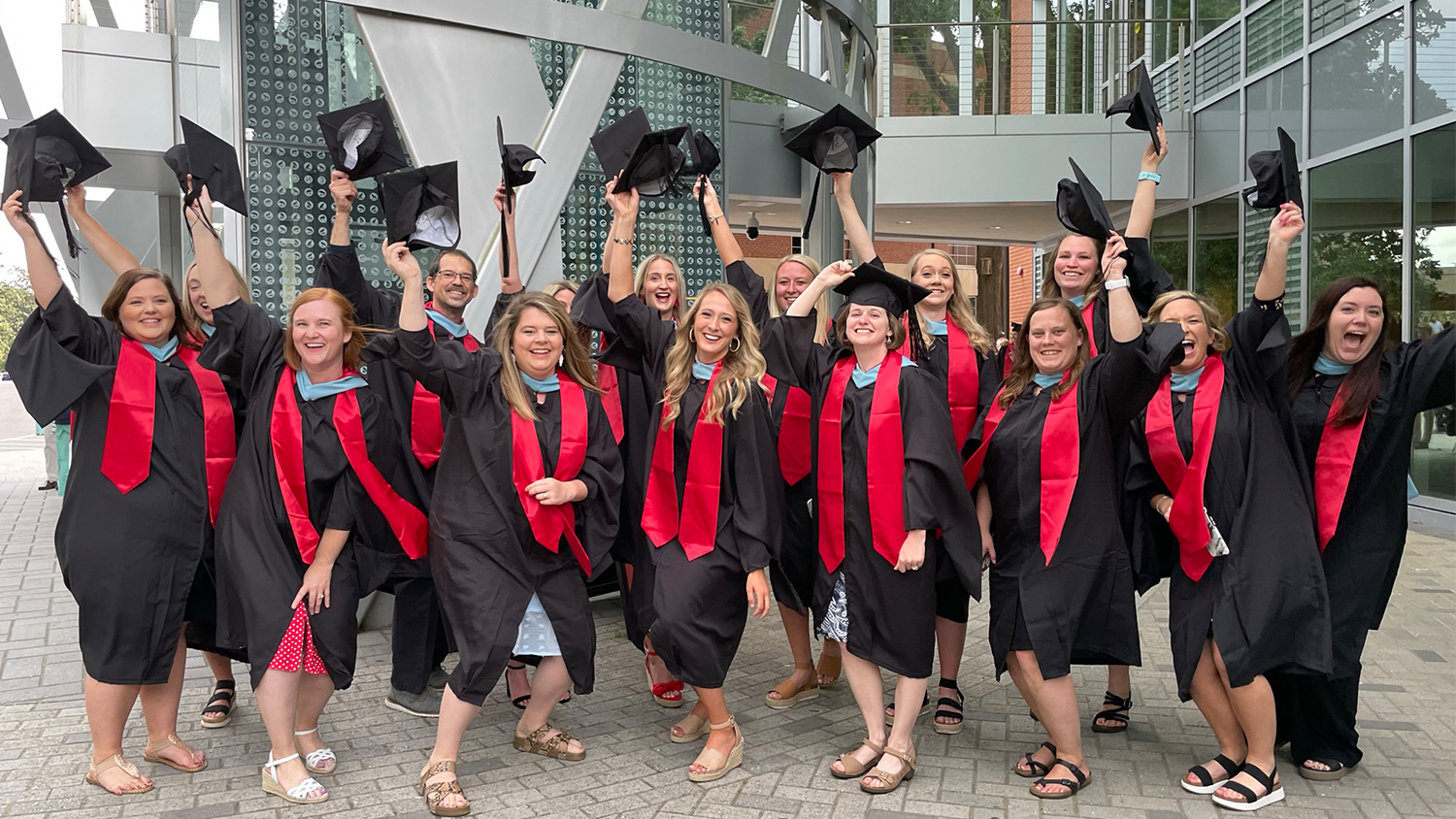 18 teachers supported by the Mebane Charitable Foundation's Yadkin Wolfpack Literacy Partnership who graduated from the College of Education with their master’s degrees in May 2022- hold their hats in the air in celebration. 